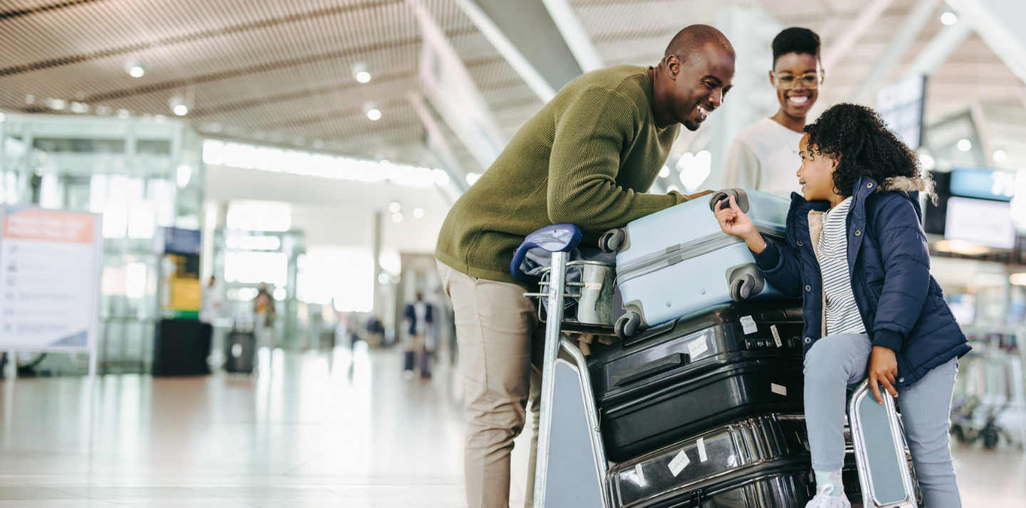 Couple in the airport with baggage travel insurance smiling with their daughter while she leans on the luggage cart