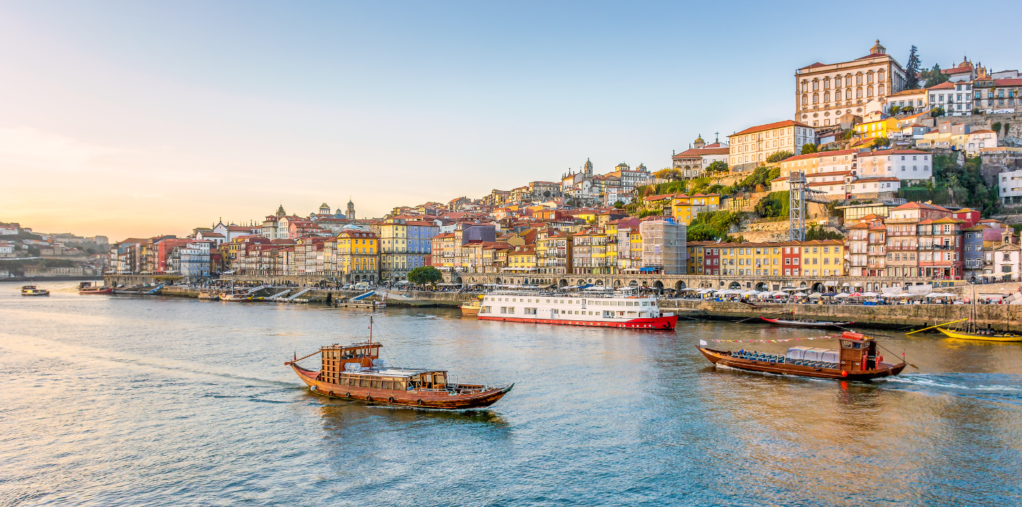 View of boats on the Duoro River and the city of Porto at sunset, where you can have travel insurance for Portugal