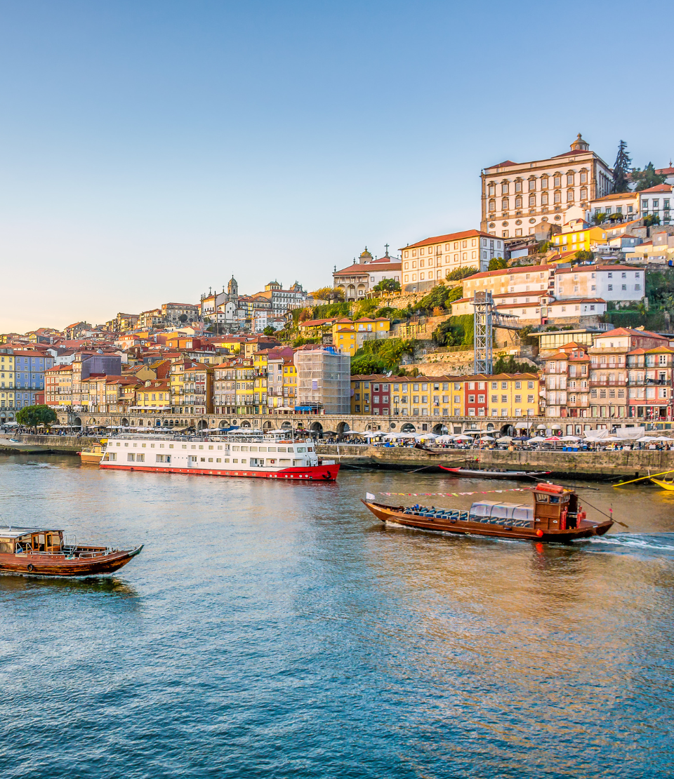View of boats on the Duoro River and the city of Porto at sunset, where you can have travel insurance for Portugal
