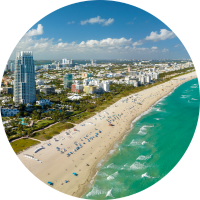 Aerial view of Miami Beach featuring the coastline with sunbathers on the sand and the city skyline in the background.