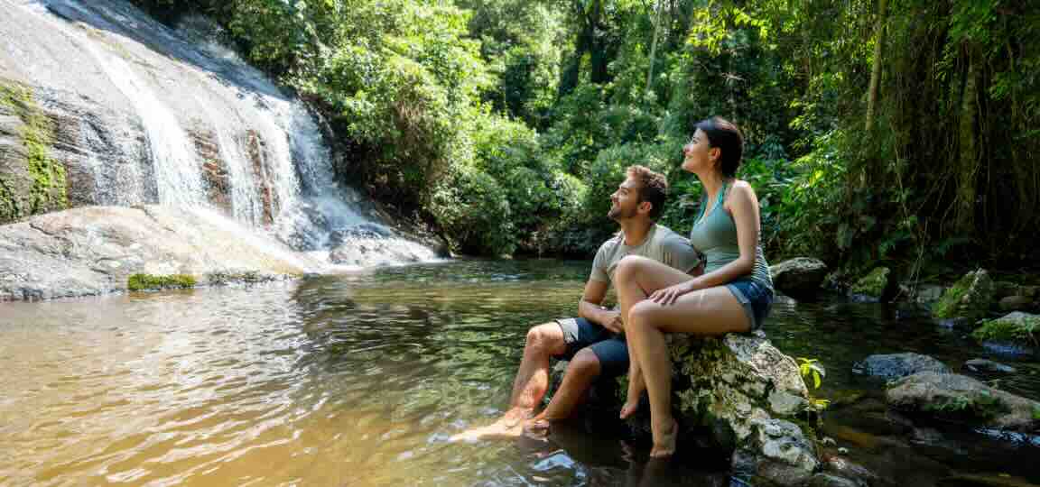 couple with travel insurance benefits sitting on rocks and looking at a waterfall in the rainforest