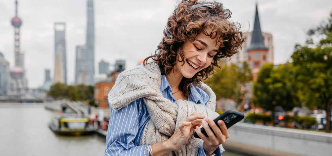 young woman using a travel app on her phone and searching different types of travel insurance in the city