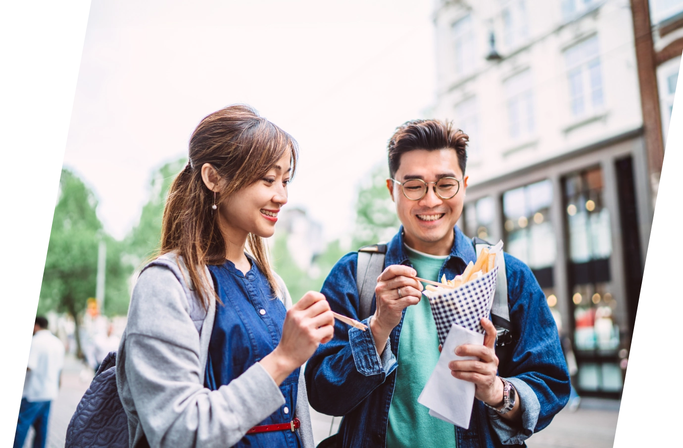 an Asian couple with long-term travel insurance enjoys street food french fries in a urban, city setting