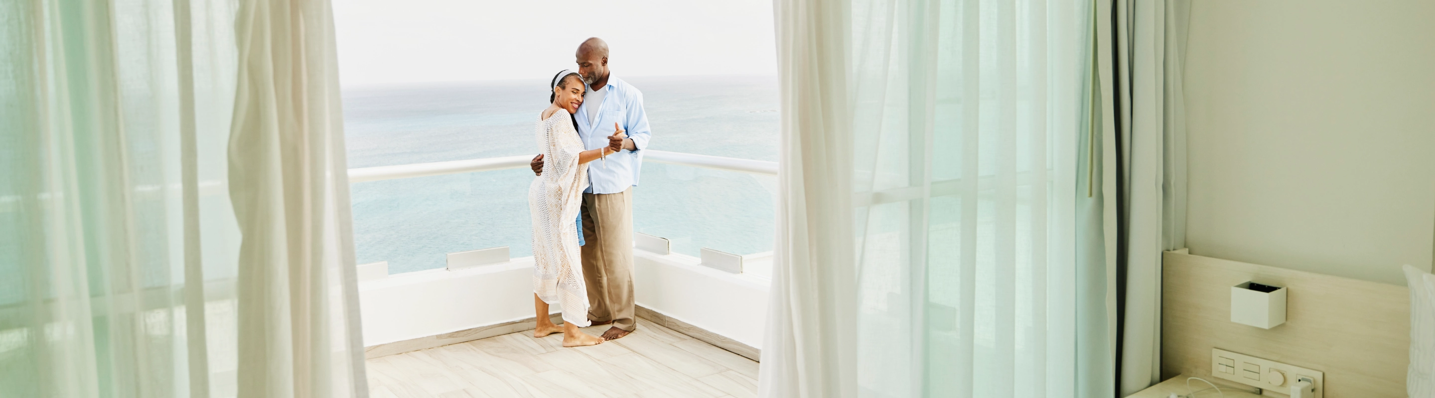 Senior couple with travel insurance for their all-inclusive vacation dancing on a hotel balcony