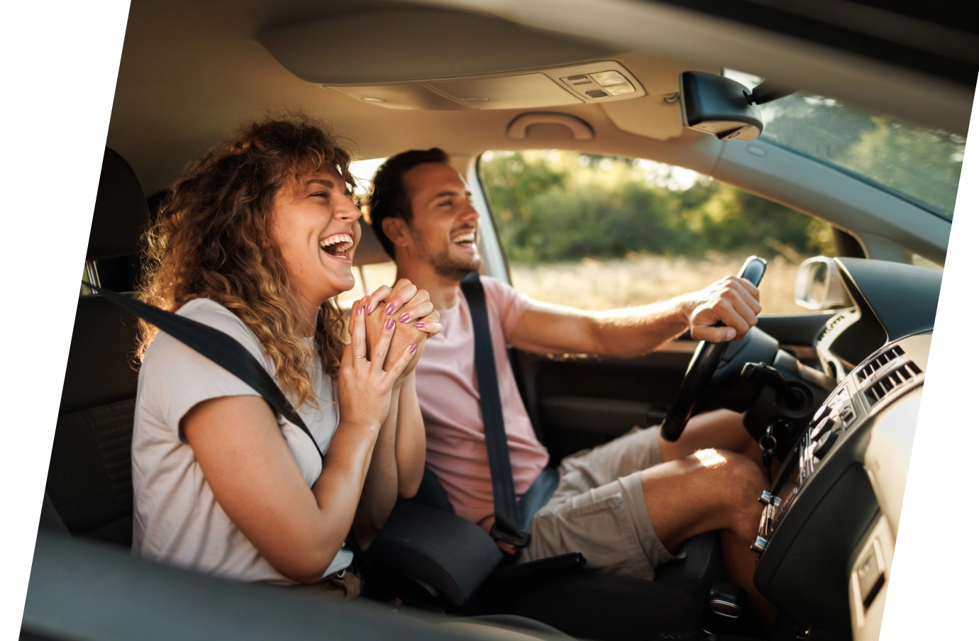 a young couple with road trip travel insurance holds hands and laughs during a car ride 