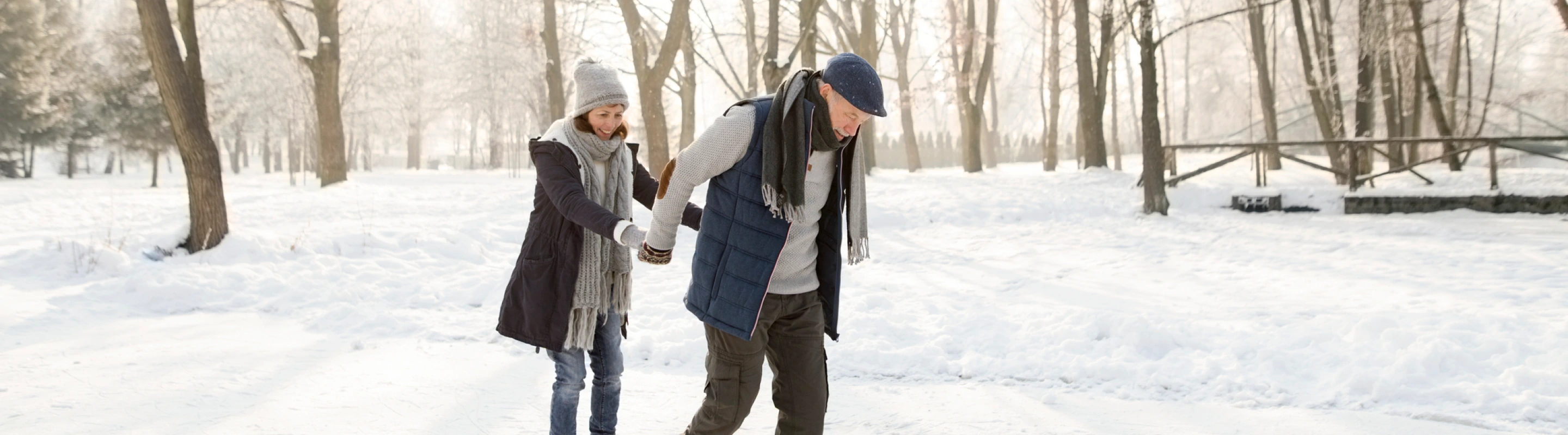 an older couple with ski insurance ice-skate outdoors in a forest setting on their winter trip, insured with ski insurance 