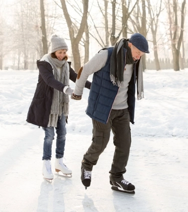 an older couple with ski insurance ice-skate outdoors in a forest setting on their winter trip, insured with ski insurance 