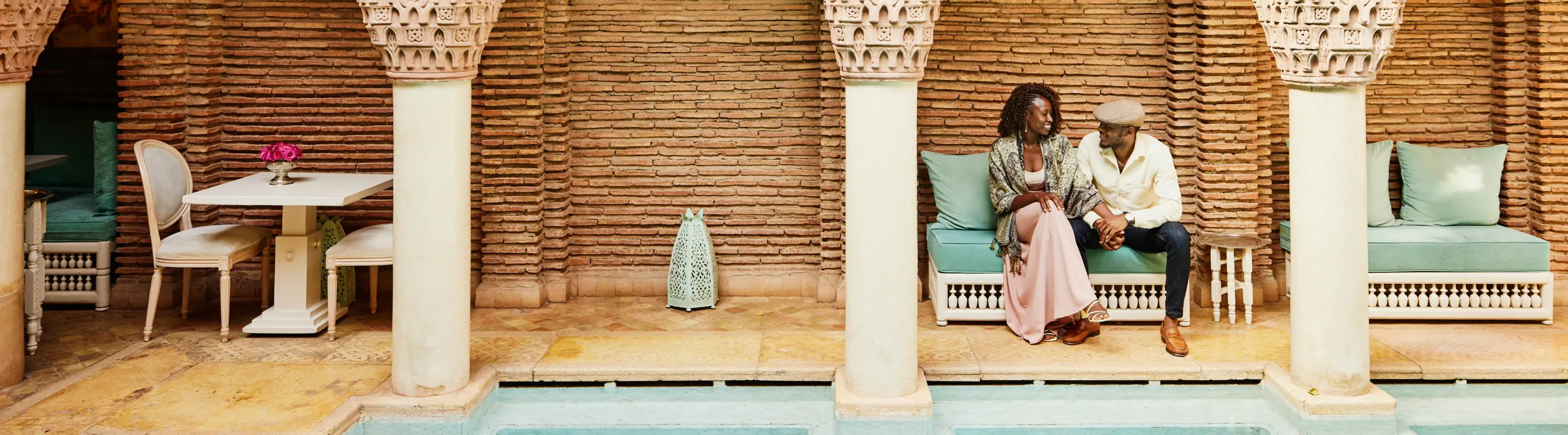 a young, Black couple with long-term travel insurance sits in a Moroccan riad-style courtyard 