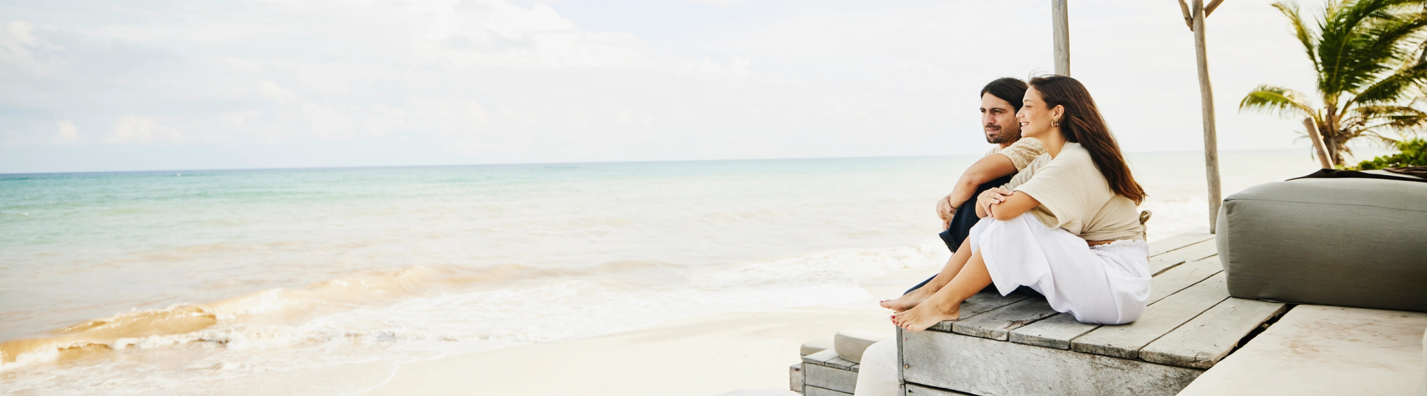 Couple with travel insurance for the Caribbean sitting on a beachfront patio and looking at the ocean