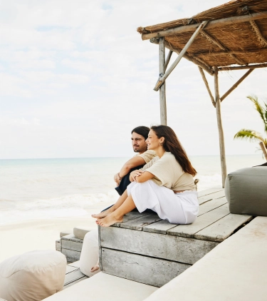 Couple with travel insurance for the Caribbean sitting on a beachfront patio and looking at the ocean