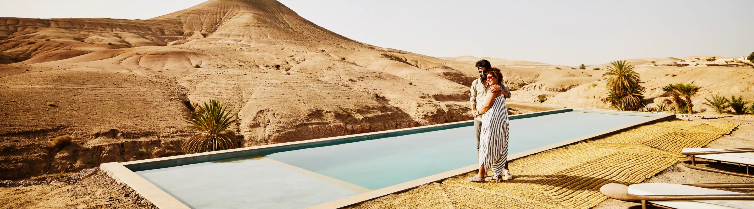 Couple walking along a pool in the desert with travel insurance for their all-inclusive vacation