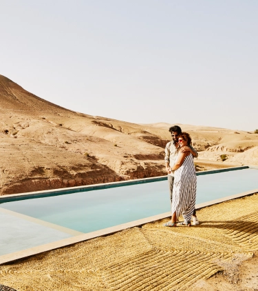 Couple walking along a pool in the desert with travel insurance for their all-inclusive vacation
