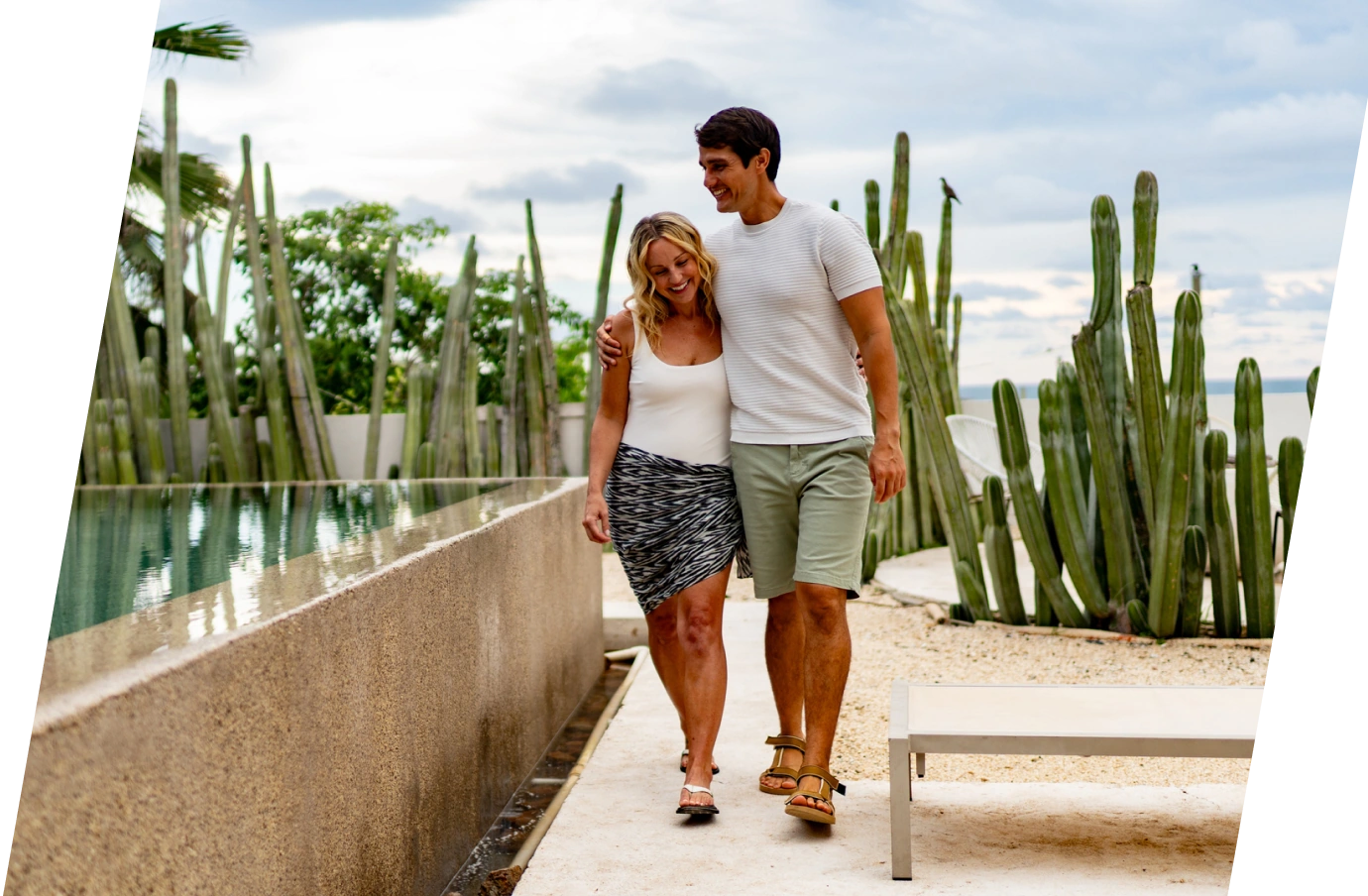 Young couple with travel insurance for Mexico embracing and walking by a pool with cacti in the background