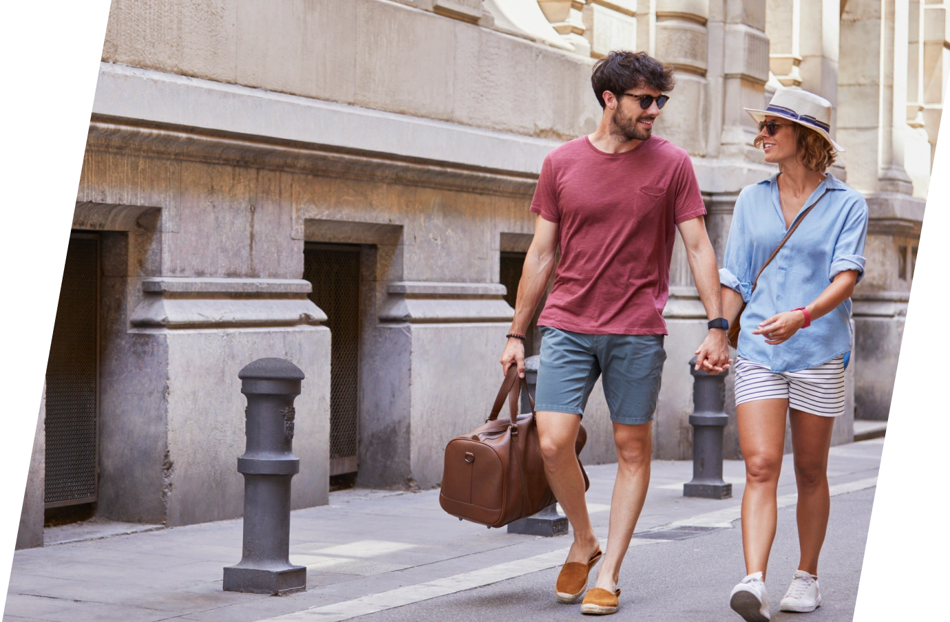 a young couple with cancel for any reason travel insurance holds hands as they walk down an urban street