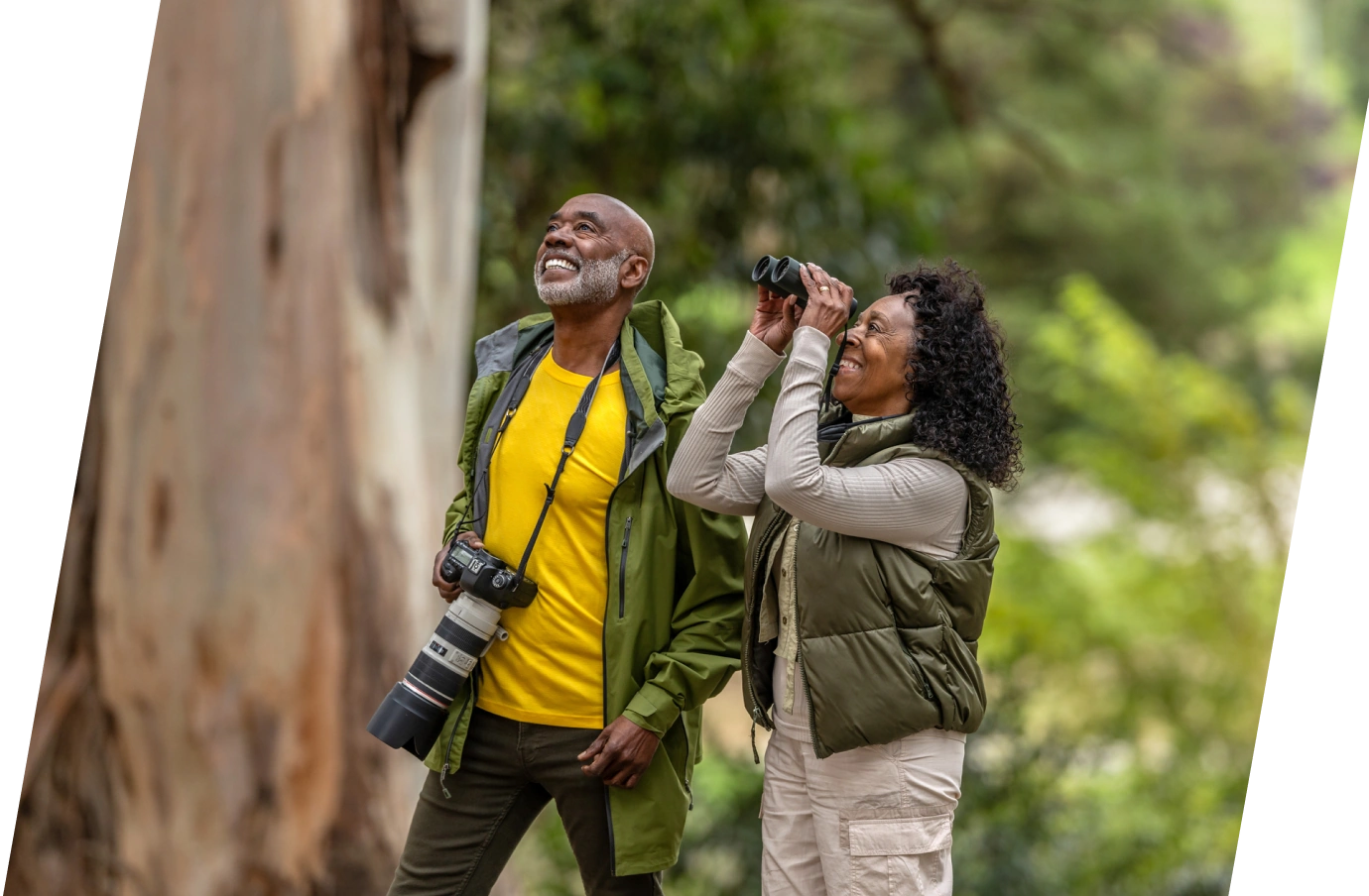an elderly black couple with travel insurance for seniors, sightseeing with their camera and binoculars in a forest 