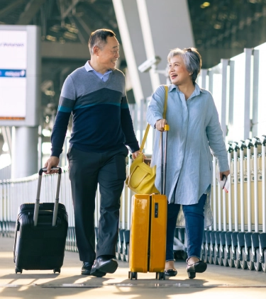 an elderly couple with travel insurance for seniors, carrying their luggage out of an airport terminal