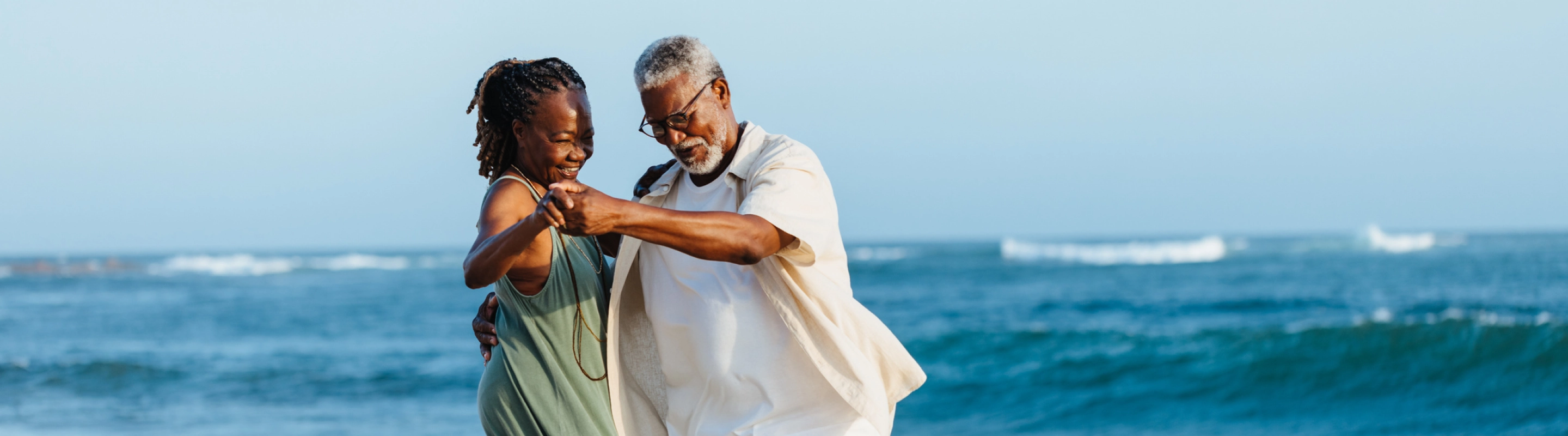 an elderly black couple dancing by the ocean with travel insurance for seniors