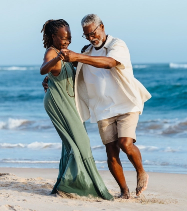 an elderly black couple dancing by the ocean with travel insurance for seniors