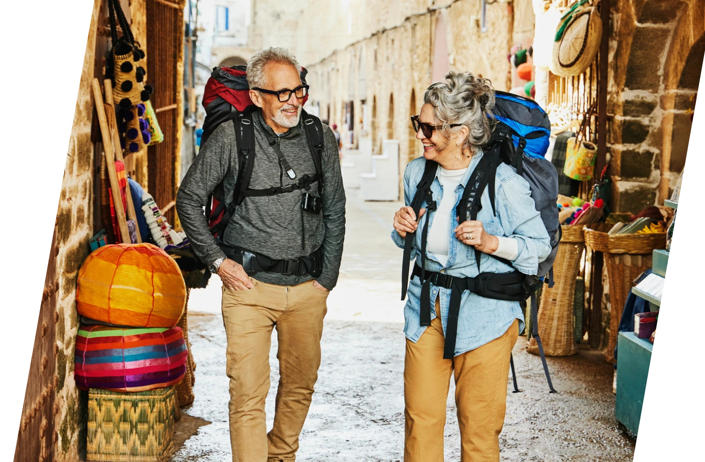an elderly couple with baggage insurance, carrying large backpacks as they explore a local market on vacation