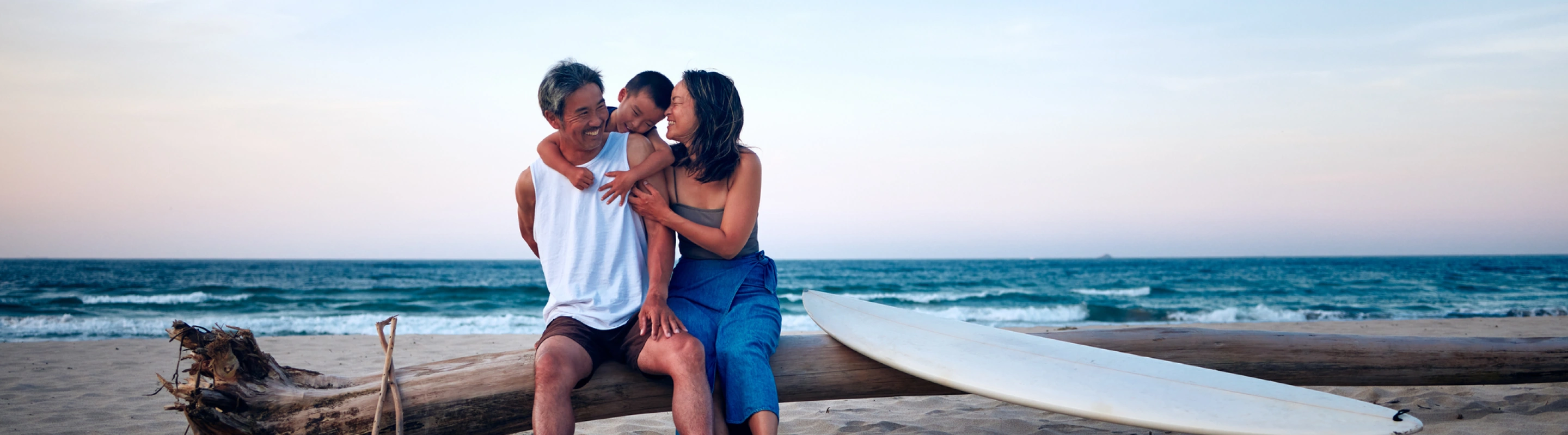 parents with inexpensive travel insurance sitting on a log on the beach with their child at sunset