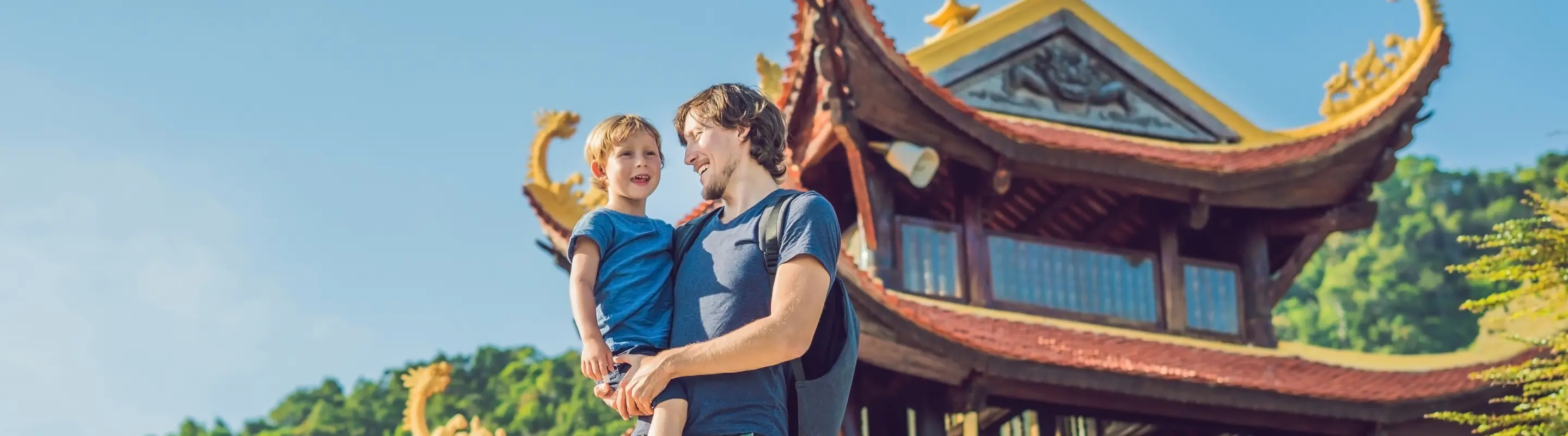 Father with travel insurance for Vietnam holding his son and smiling in front of a Buddhist temple in Phu Quoc
