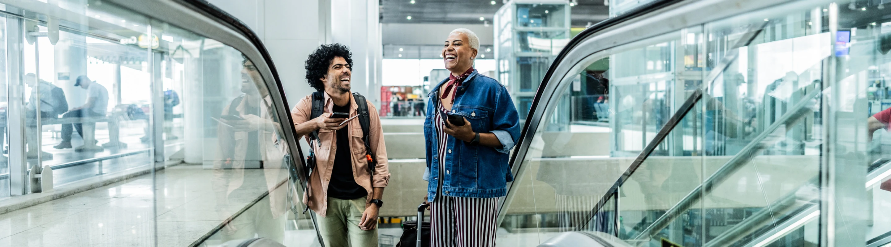 a man and woman with accidental death travel insurance, laughing as they take an escalator at an airport 