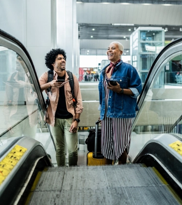 a man and woman with accidental death travel insurance, laughing as they take an escalator at an airport 