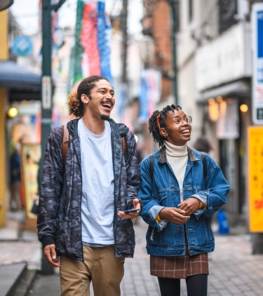 two friends with travel insurance for Japan, laughing as they walk through Tokyo 