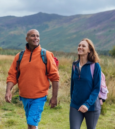 a young, interracial couple with backpacker travel insurance smiles as they hike through grassy terrain