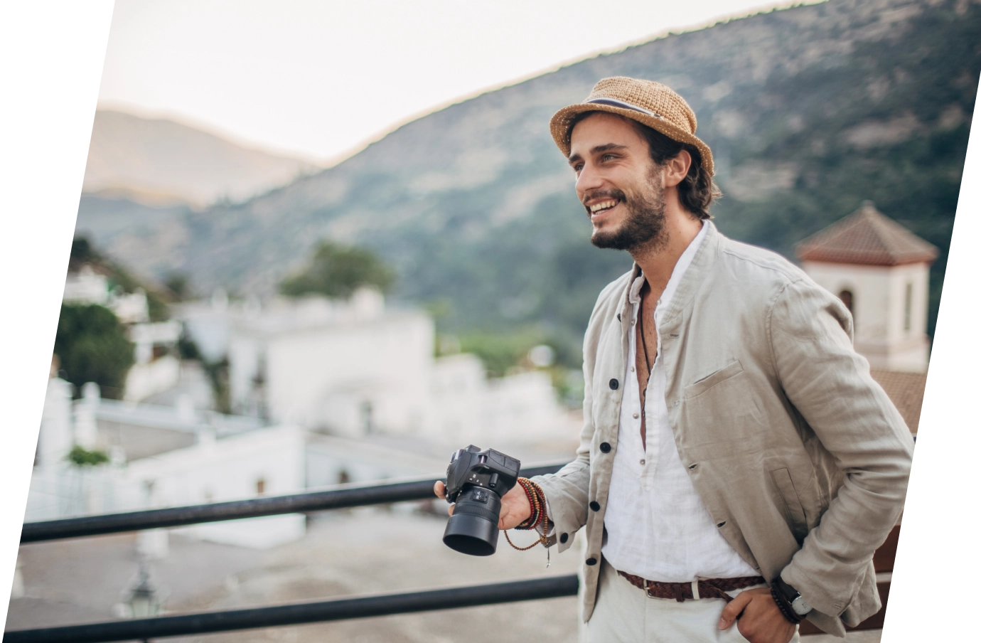 a young man with long-term travel insurance holds a photographer camera on a terrace overlooking a hillside village 