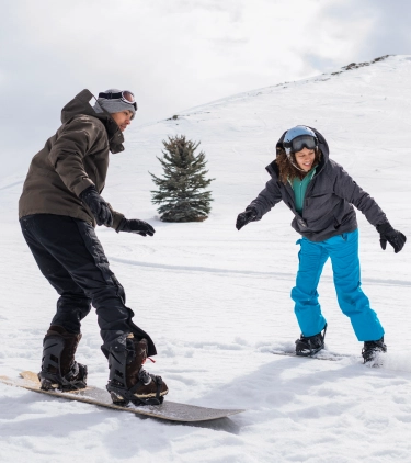 a young man and woman snowboard down a snowy slope on a winter vacation after researching snowboard and ski insurance