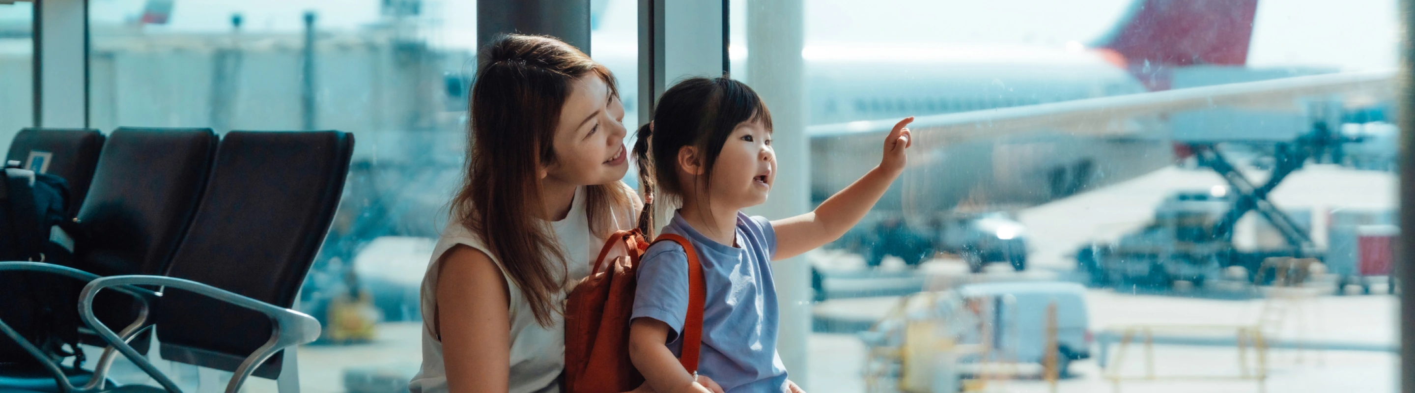a mother-daughter duo with family travel insurance, looking at airplanes at the airport