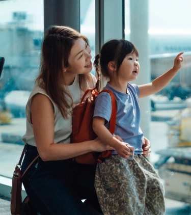 a mother-daughter duo with family travel insurance, looking at airplanes at the airport