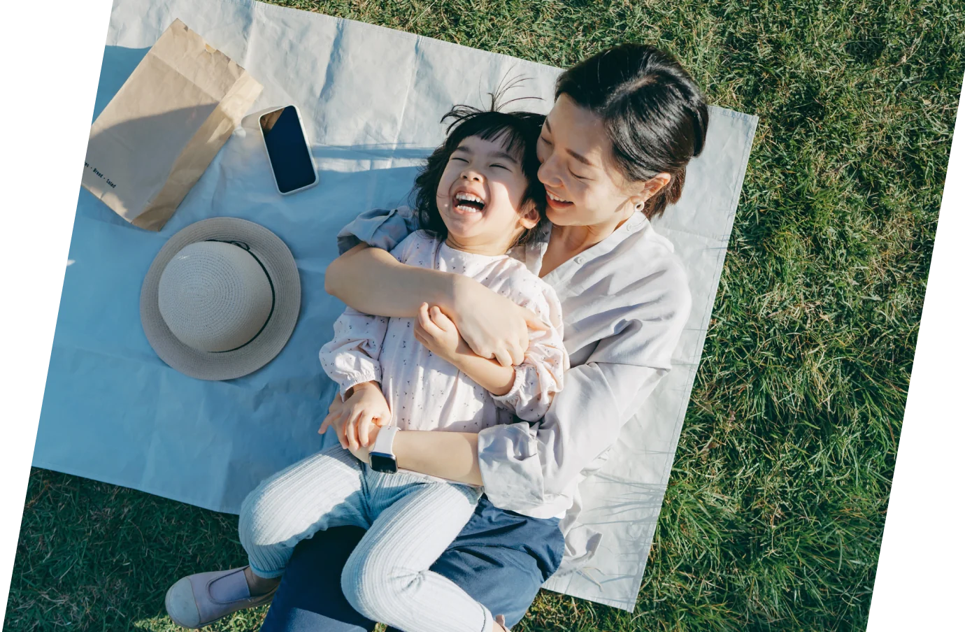 a mother and daughter with travel insurance for COVID-19 embrace on a blanket on the grass 