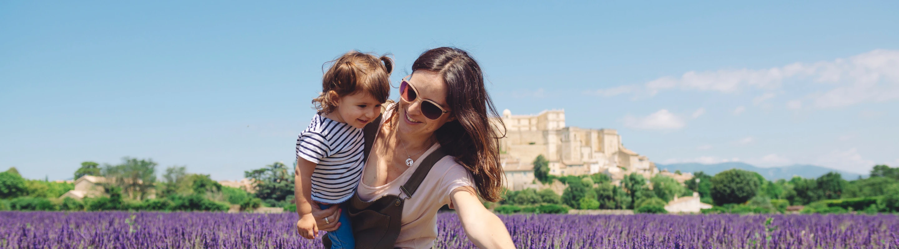 Mother with travel insurance for France holding her young daughter in a lavender field with a historic building in the background