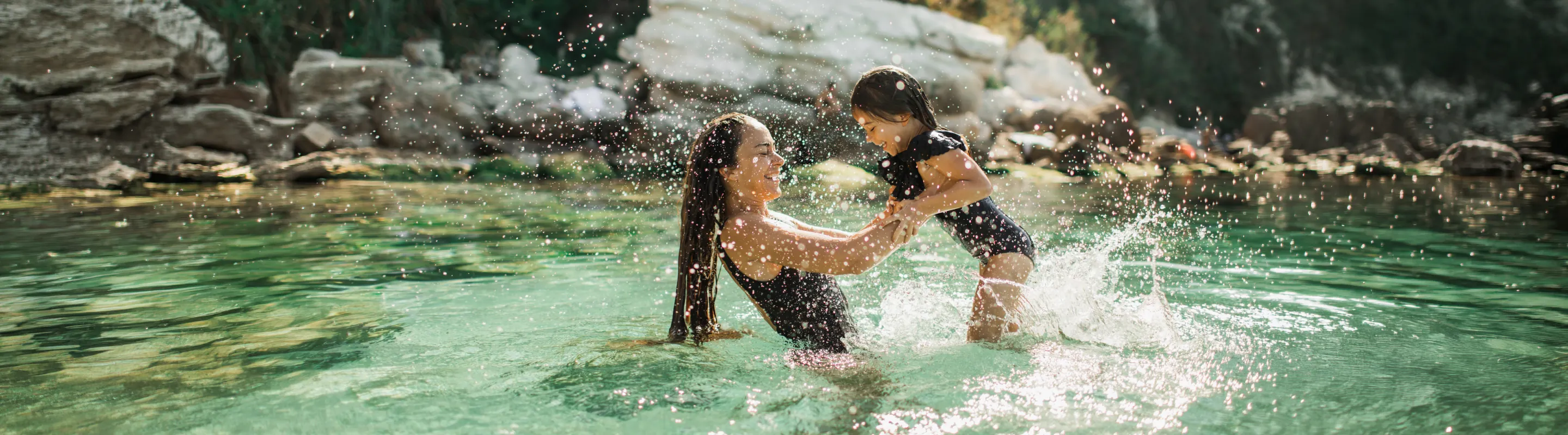 Mother with travel insurance for the Caribbean holding her young daughter and splashing in the ocean