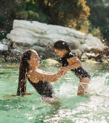Mother with travel insurance for the Caribbean holding her young daughter and splashing in the ocean