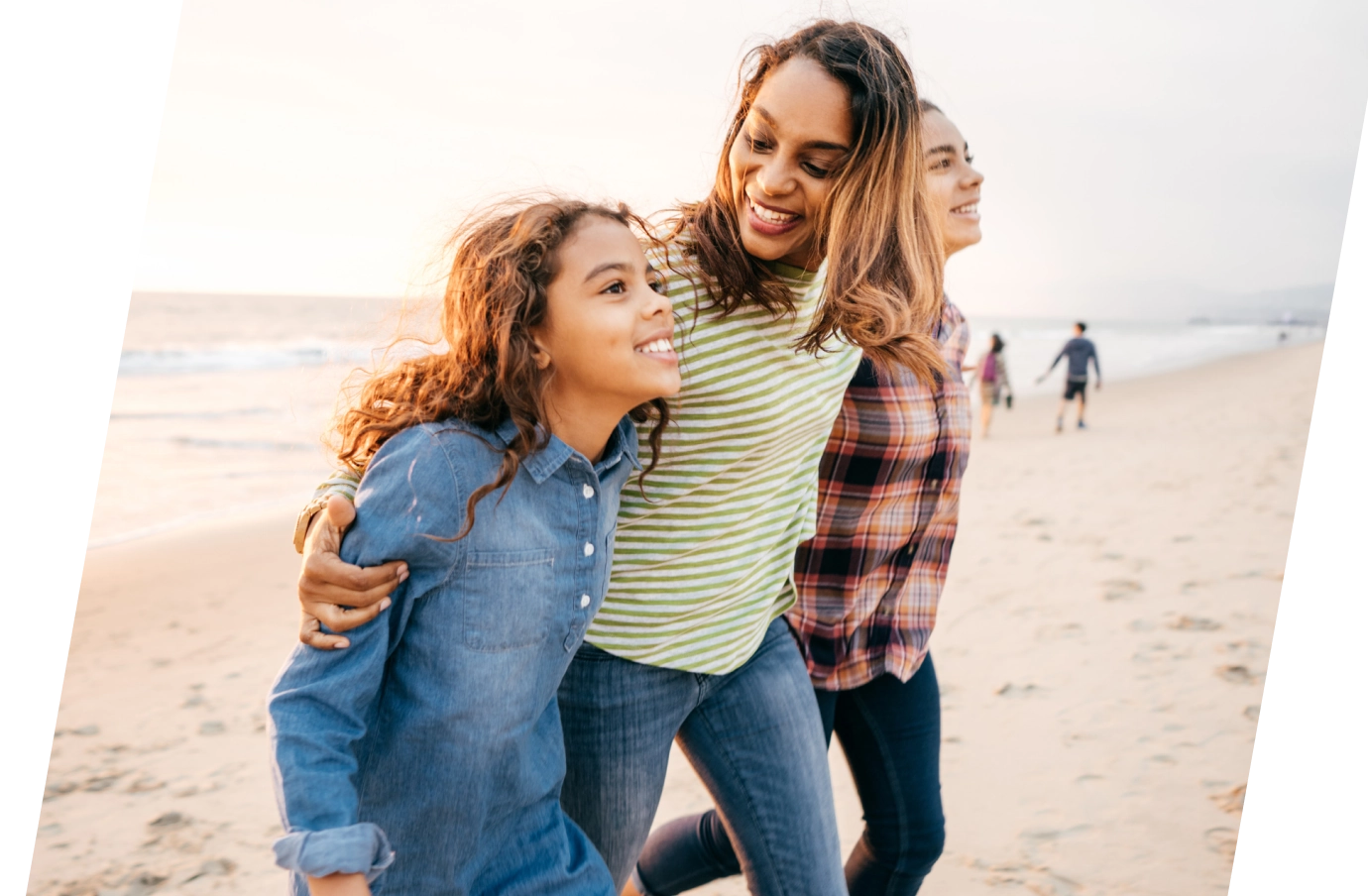 a mother wraps her arms around her two daughters at the beach on vacation, all insured with family travel insurance
