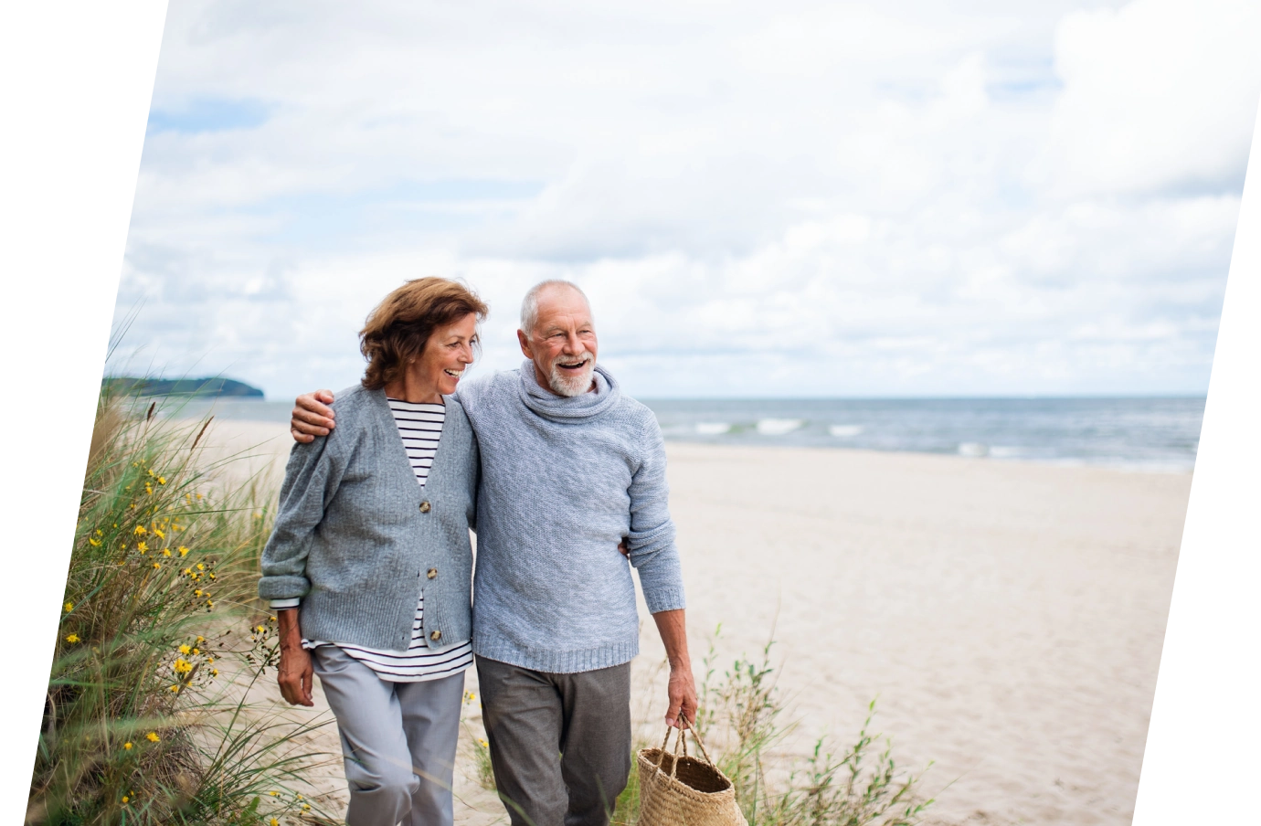 an older couple with travel insurance for beach trips holds hands as they enjoy a walk in the sand by the ocean 