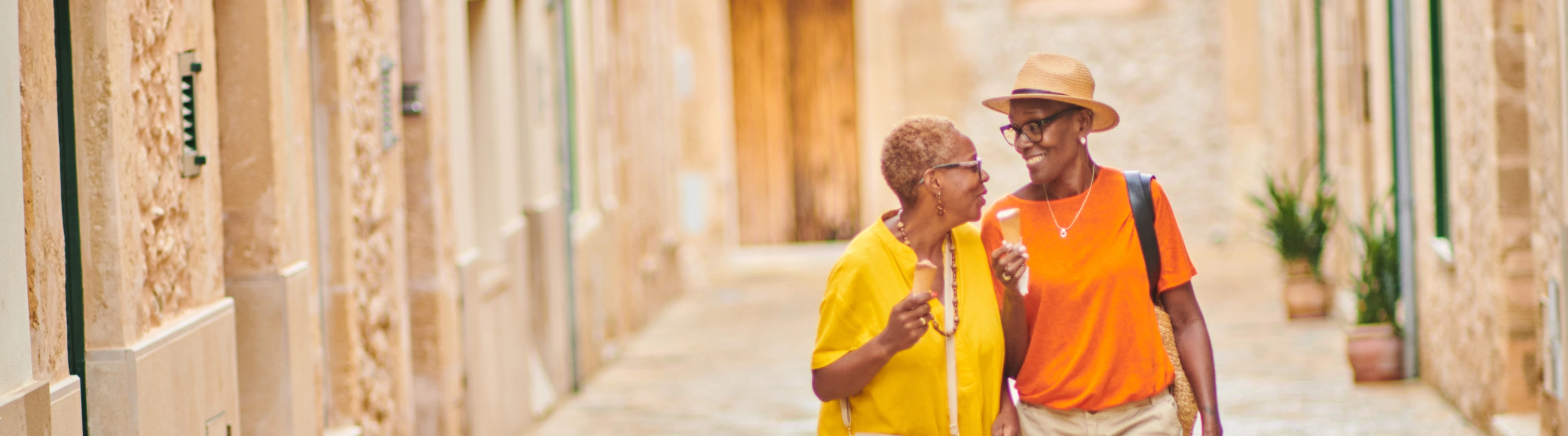 an older couple with LGBTQ+ travel insurance walks down a cobblestone street while enjoying ice cream
