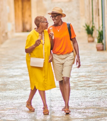 an older couple with LGBTQ+ travel insurance walks down a cobblestone street while enjoying ice cream