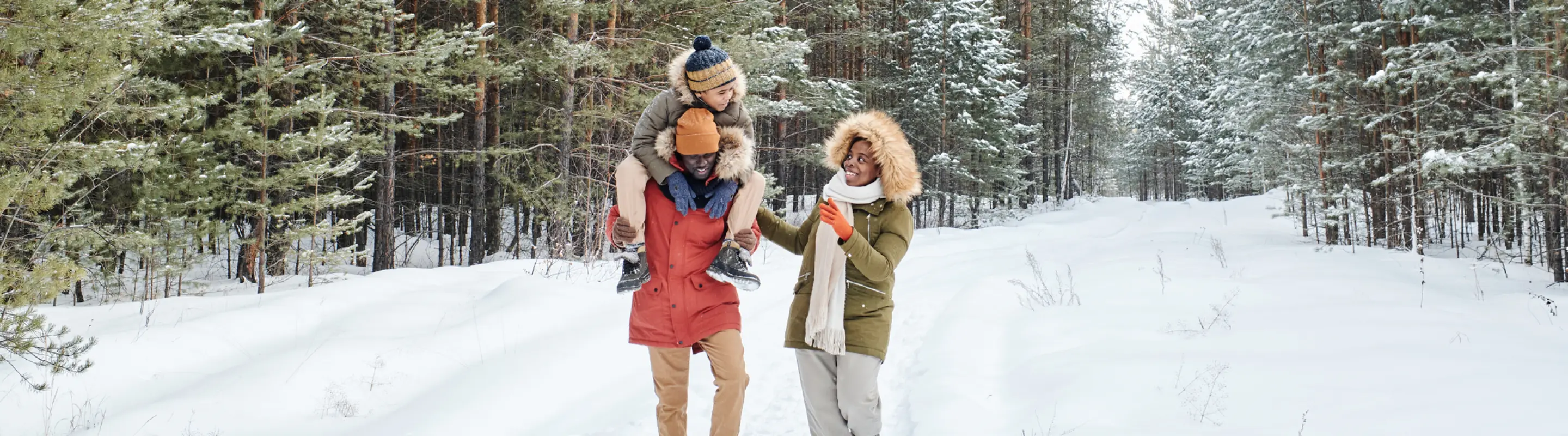 two young, mixed-race parents and their child walk through a snowy forest on a winter trip after researching ski insurance 