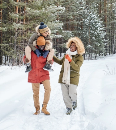 two young, mixed-race parents and their child walk through a snowy forest on a winter trip after researching ski insurance 
