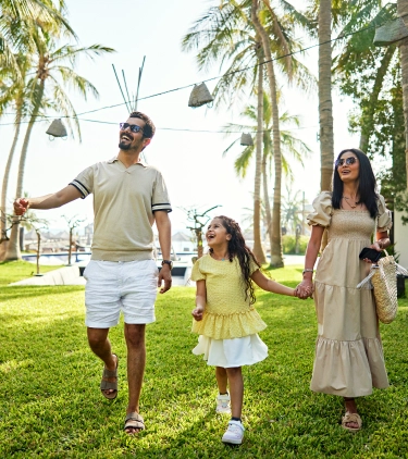 two young parents with long-term travel insurance walk alongside their daughter through a tropical resort with palm trees