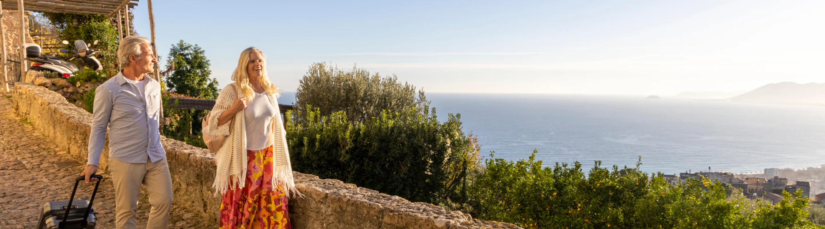 Senior couple with travel insurance for Italy walking down a cobblestone street overlooking the ocean