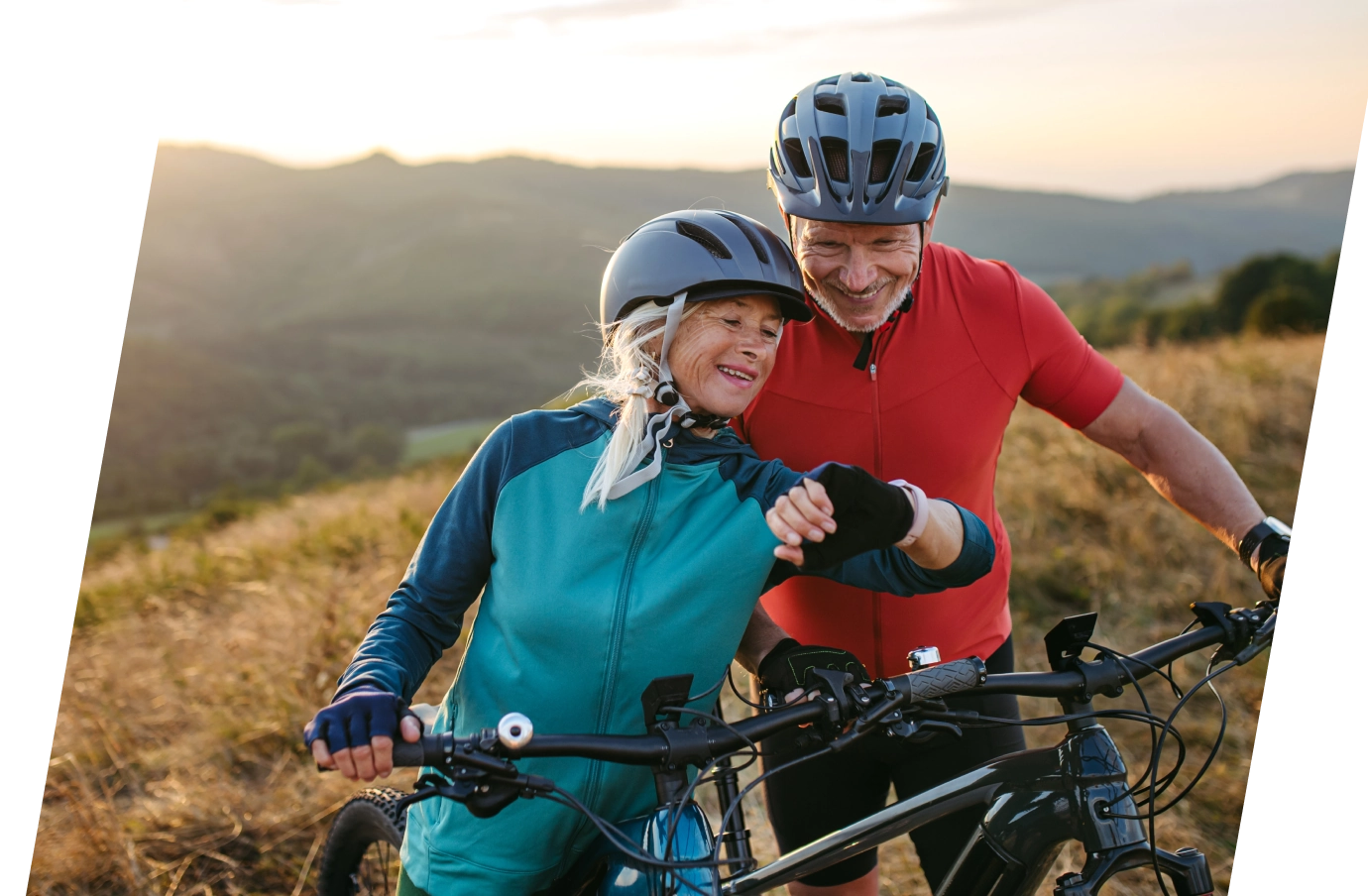 Senior couple checking smart watch while mountain biking on a grassy hill with Travelex customer service
