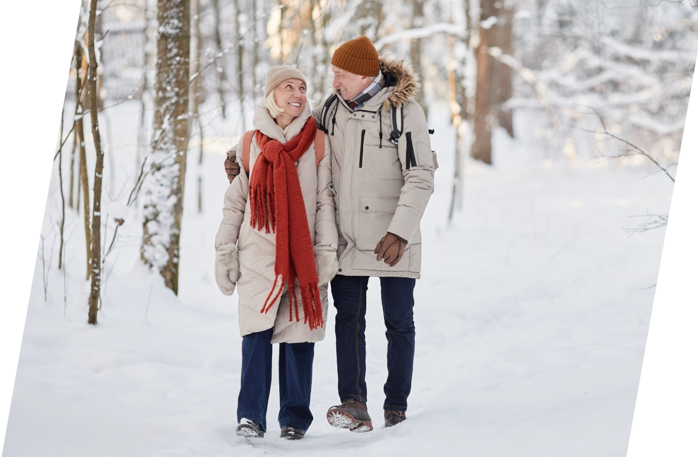 Senior couple in the Travelex affiliate program smiling at each other while walking through a snowy forest