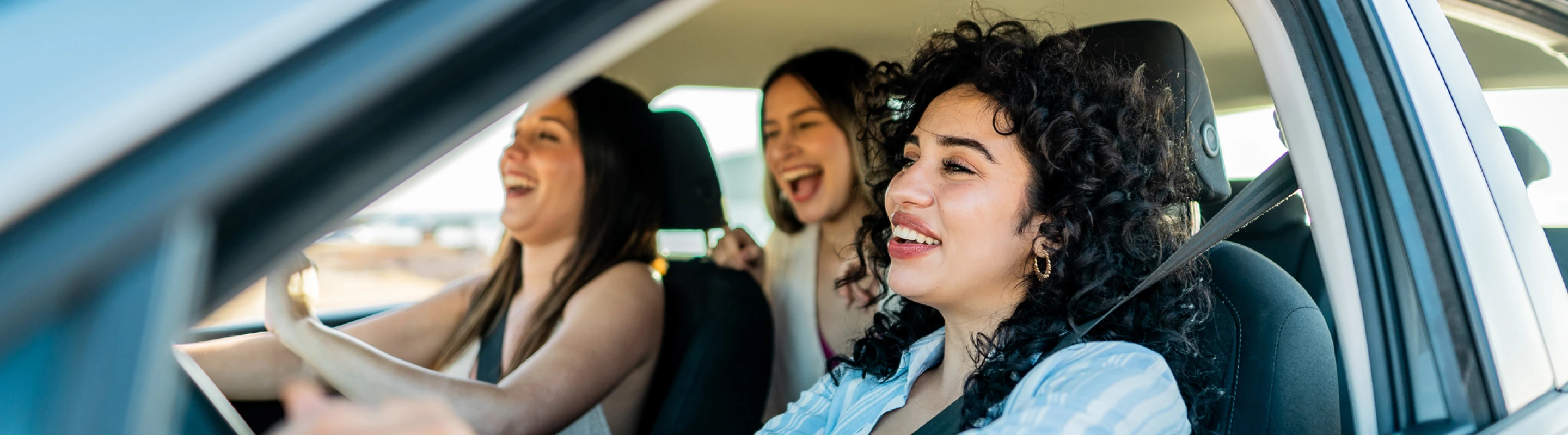 three young women friends laugh inside a car vacation, insured with road trip travel insurance 