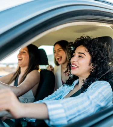 three young women friends laugh inside a car vacation, insured with road trip travel insurance 