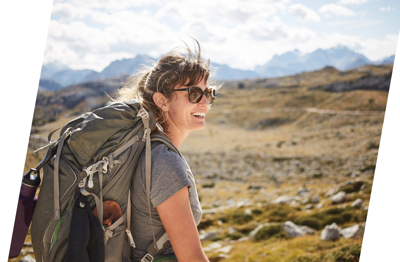 a young woman wearing sunglasses hikes through rocky alpine terrain, insured with backpacker travel insurance 